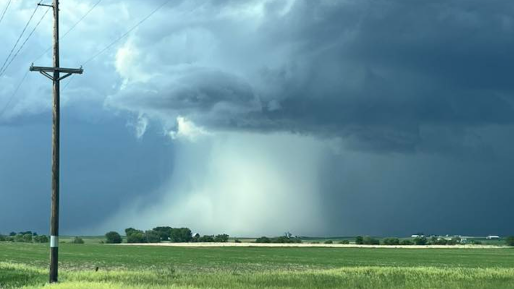What is a downburst - IowaWeather.com Wooden utility pole in a green field as a severe thunderstorm brews, with a funnel-like rain shaft reaching toward the ground in the distance.