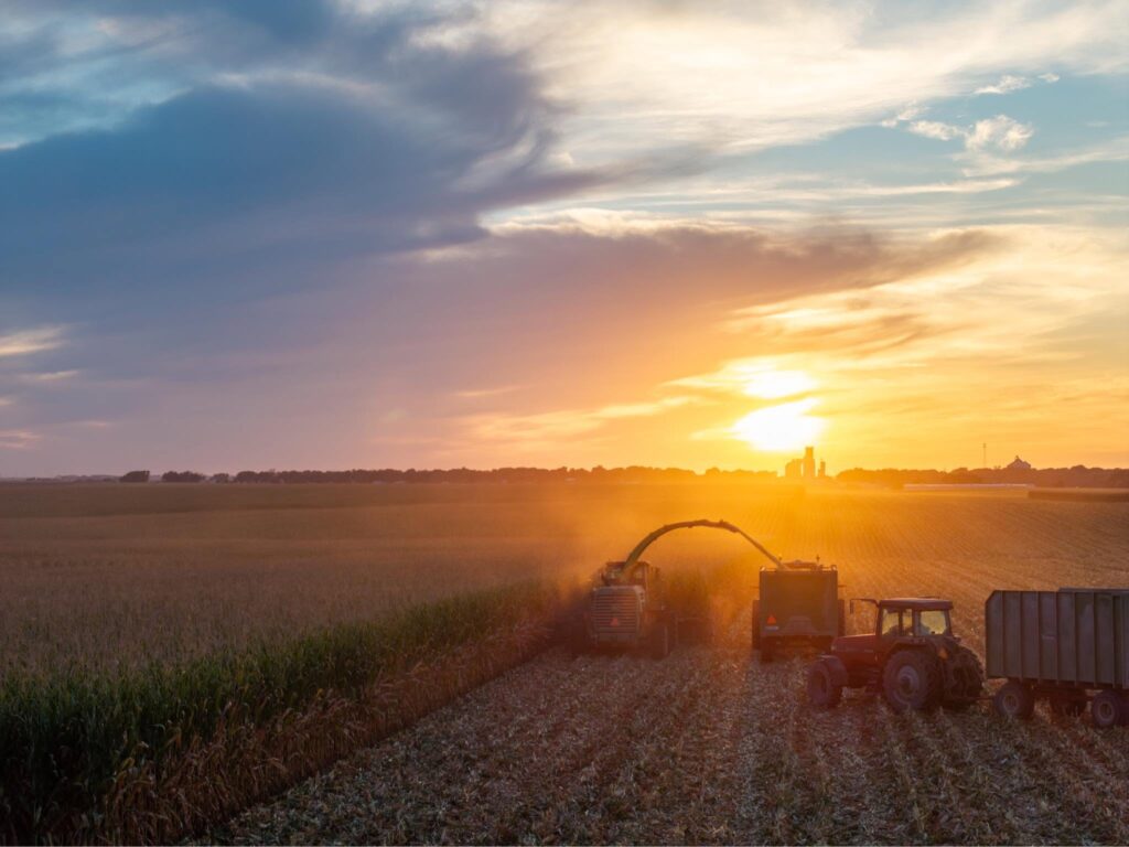 Fall in Iowa - IowaWeather.com Farm machinery and tractors in a harvested field at sunset, warm orange light on the horizon.