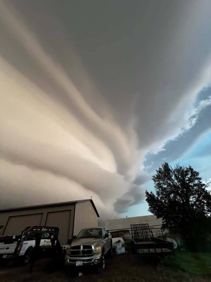 Stockton Iowa Shelf Cloud - IowaWeather.com Massive, layered storm cloud looming over a rural industrial yard with trucks and a warehouse.